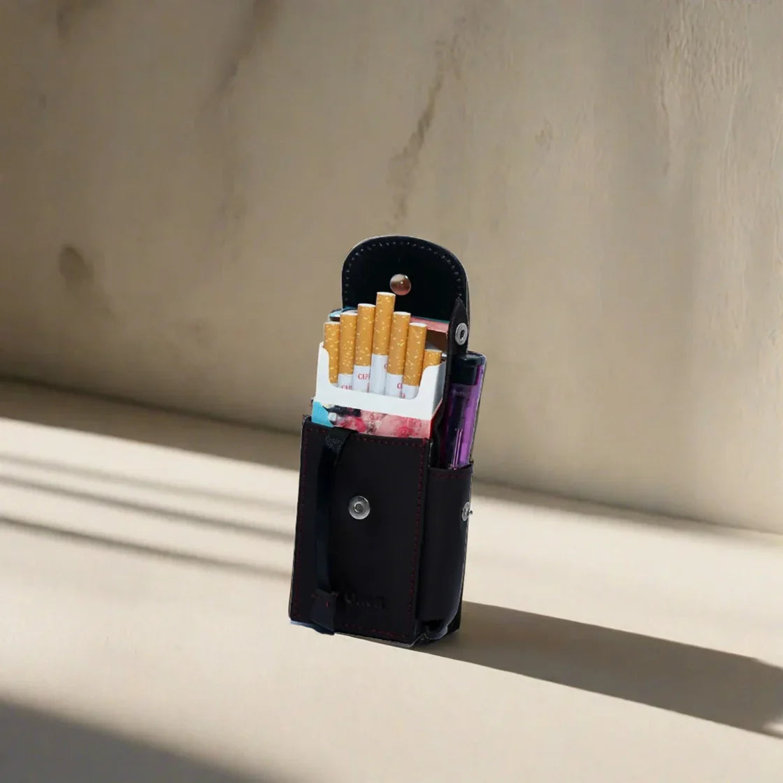 Black leather cigarette case with cigarettes and a pack of Marlboro cigarettes on a beige surface.